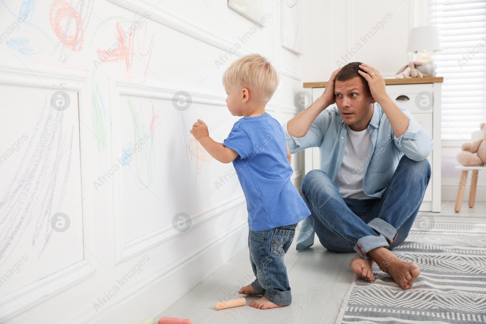 Photo of Frustrated father watching his little son drawing on wall at home