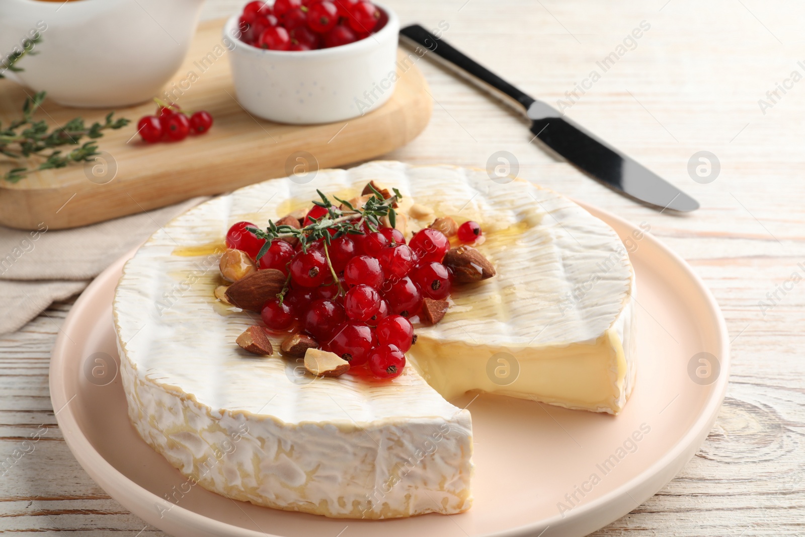 Photo of Brie cheese served with almonds, red currants and honey on white wooden table, closeup