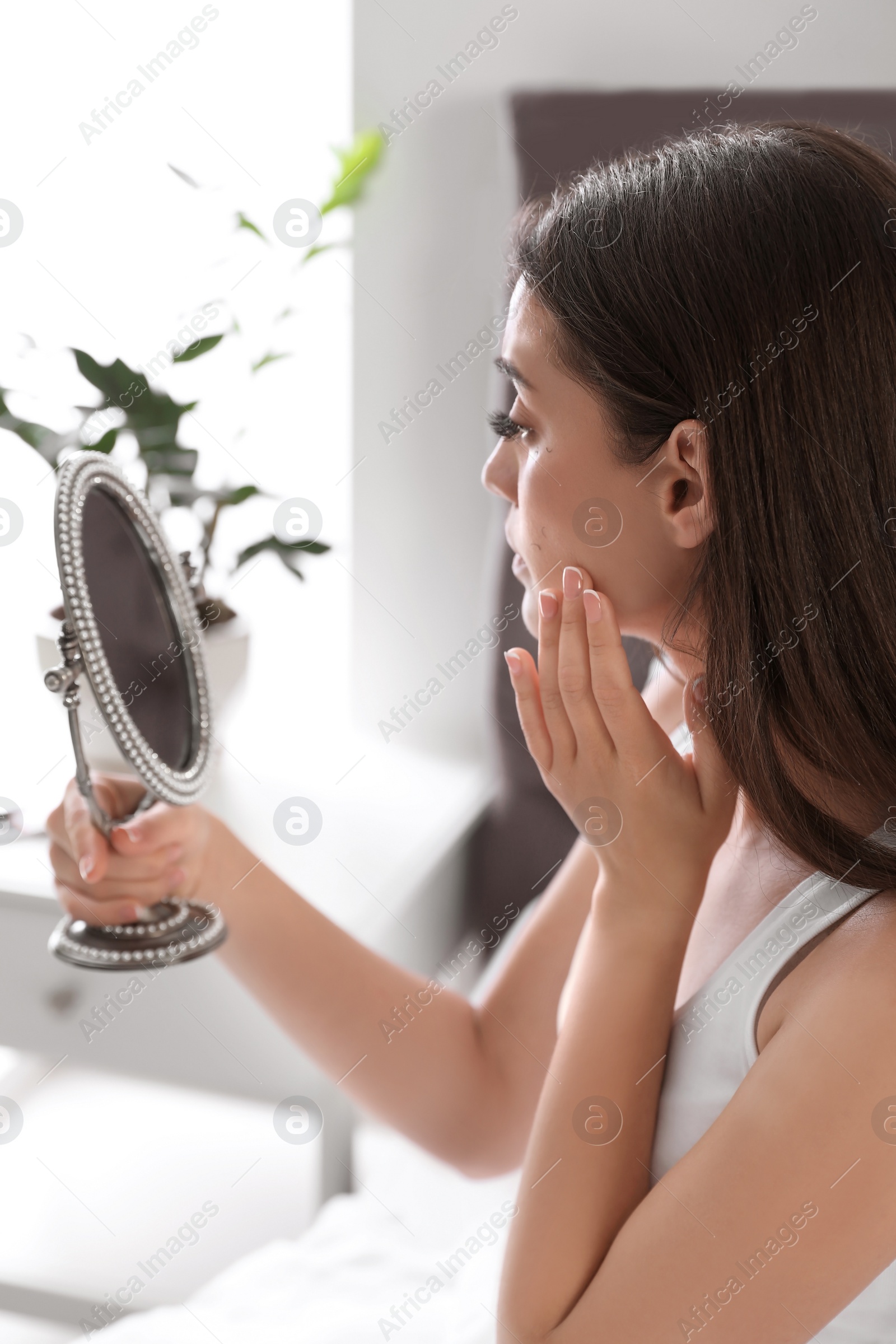 Photo of Young woman with eyelash loss problem looking in mirror indoors