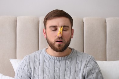 Photo of Young man with clothespin suffering from runny nose in bed indoors