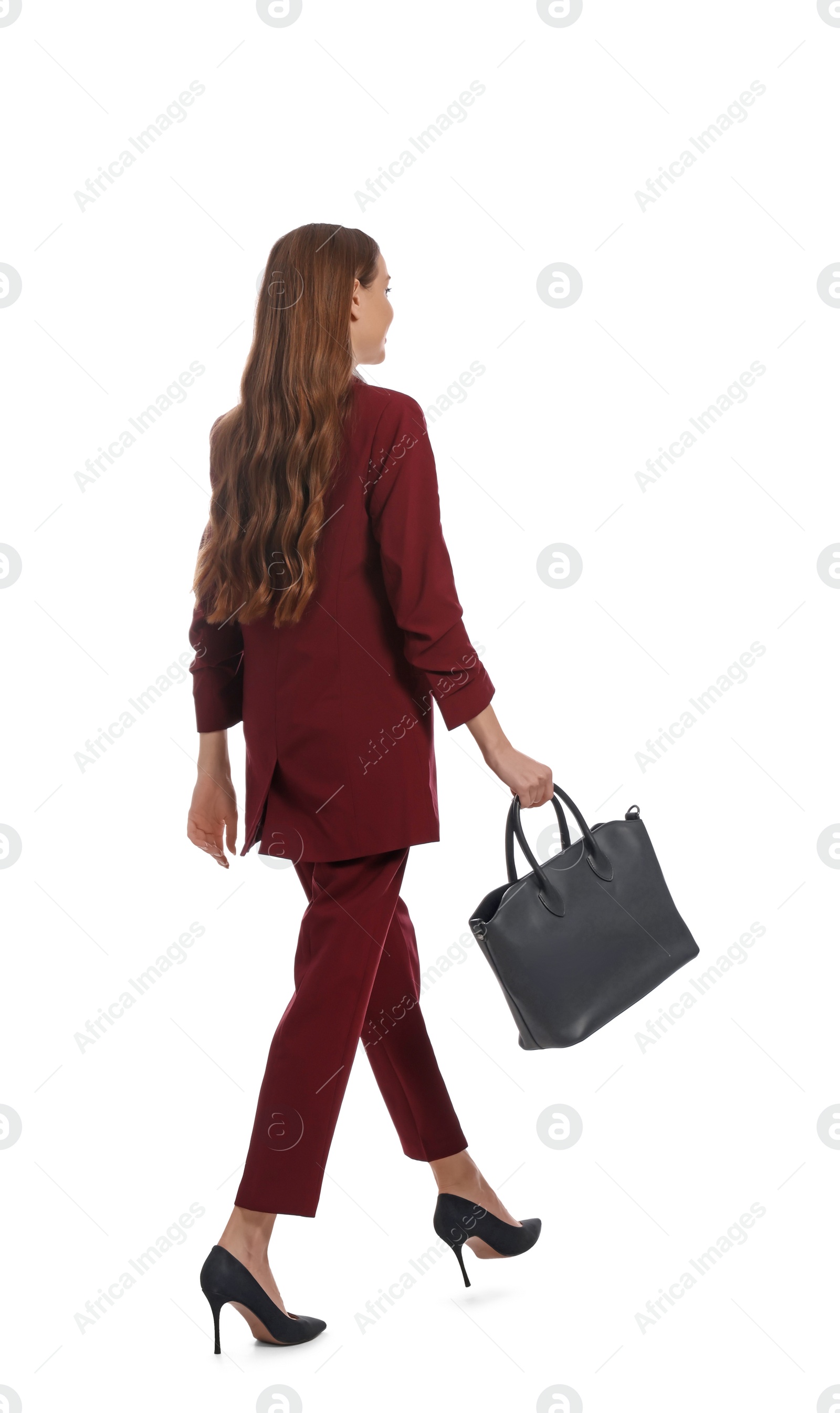 Photo of Young woman in burgundy suit with black bag walking on white background