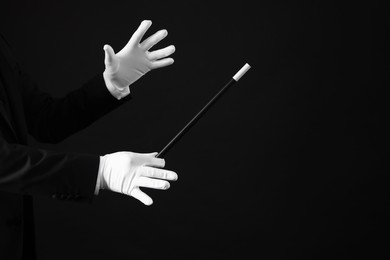 Magician holding wand on black background, closeup. Space for text