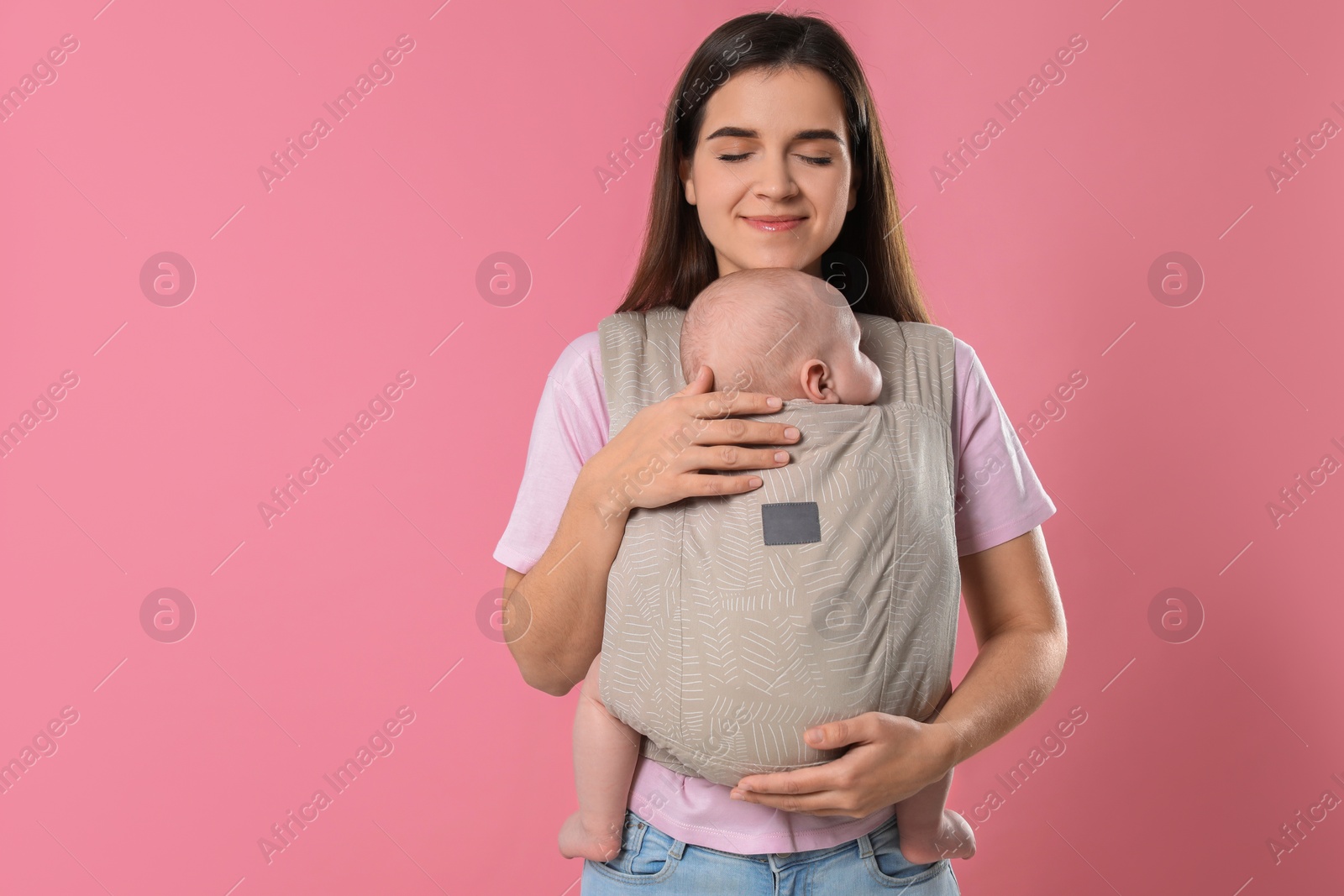 Photo of Mother holding her child in sling (baby carrier) on pink background. Space for text