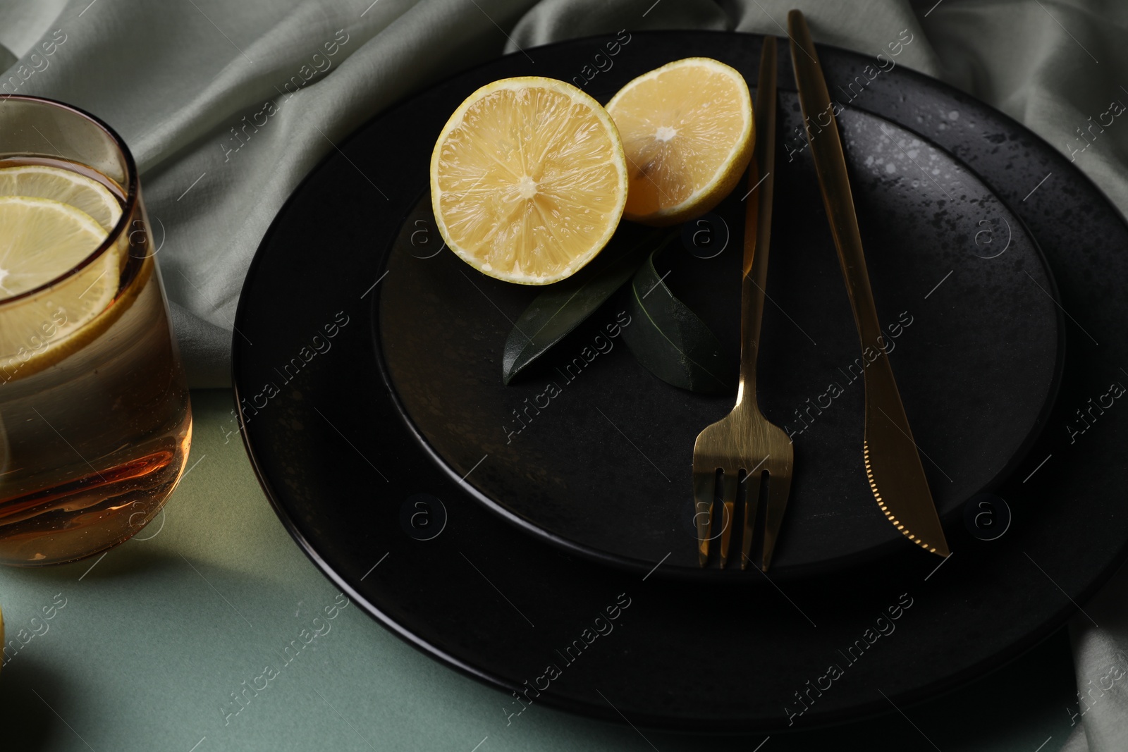 Photo of Stylish table setting. Plates, cutlery and tea with lemon on olive background, closeup