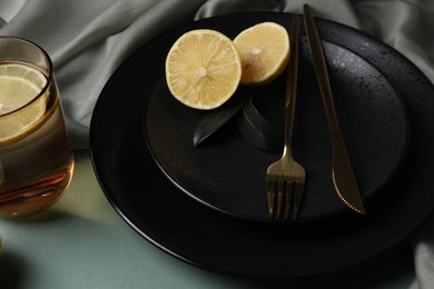 Stylish table setting. Plates, cutlery and tea with lemon on olive background, closeup