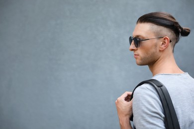 Photo of Handsome young man in stylish sunglasses with backpack near grey wall, space for text