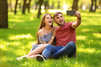 Happy young couple taking selfie on green grass in park