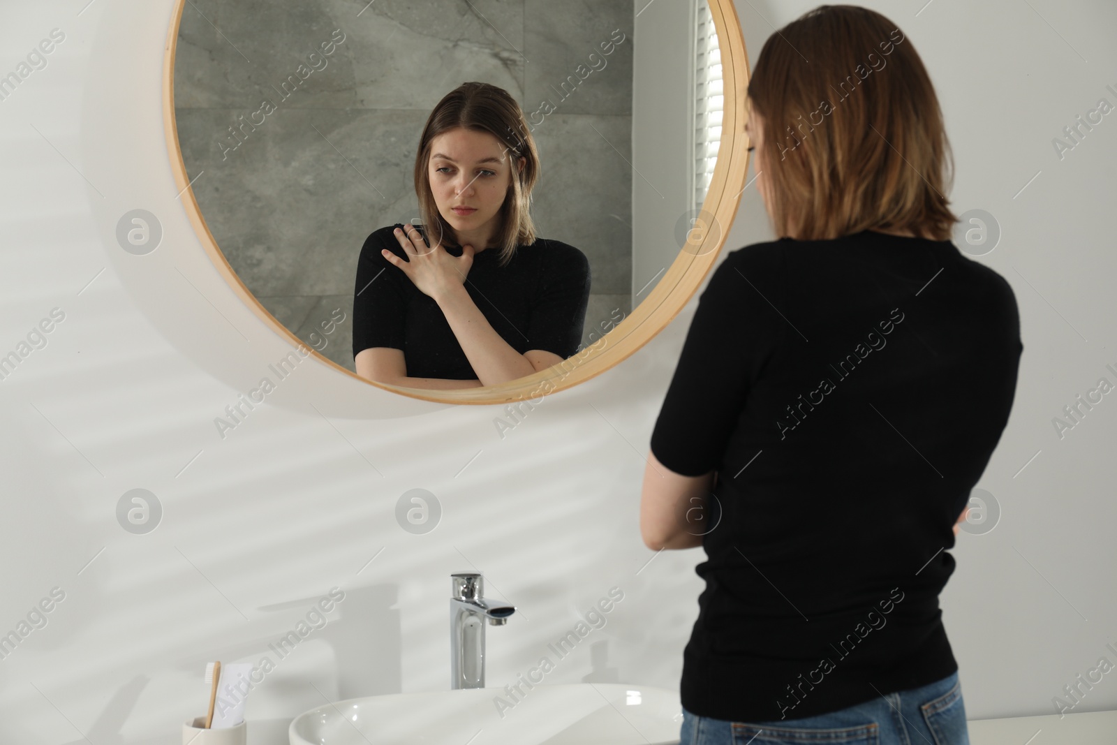 Photo of Sad young woman near mirror in bathroom
