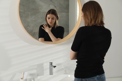Sad young woman near mirror in bathroom