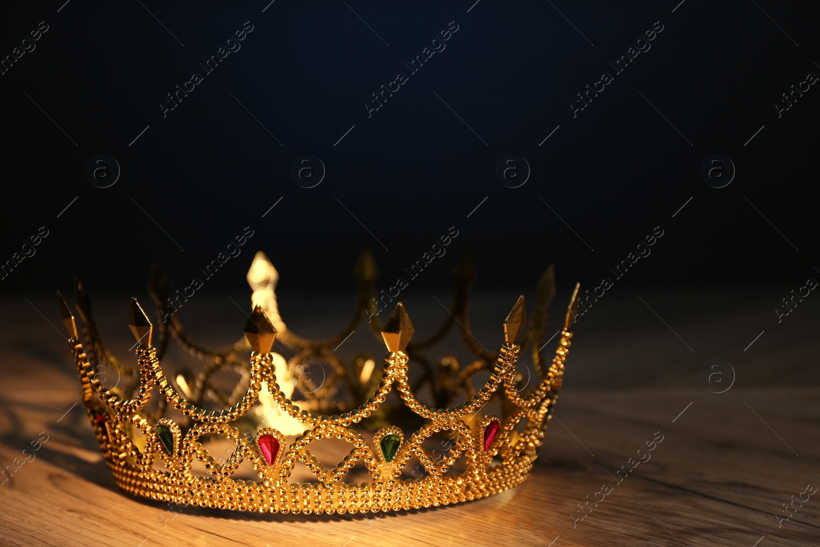 Photo of Beautiful golden crown with gems on wooden table. Fantasy item