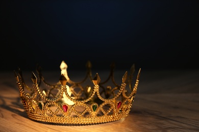 Photo of Beautiful golden crown with gems on wooden table. Fantasy item