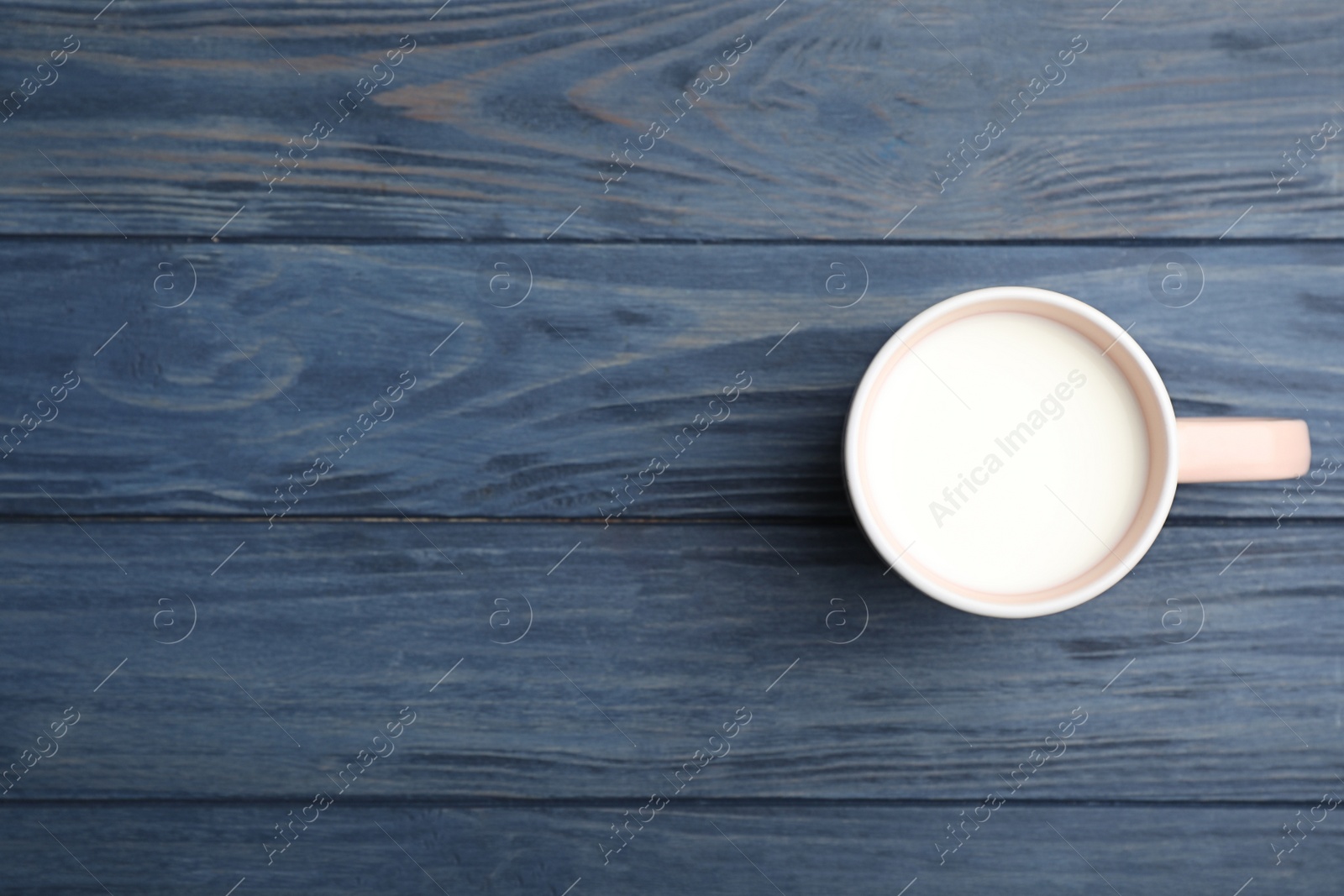 Photo of Cup of fresh milk on wooden table, top view. Space for text