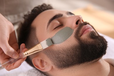 Photo of Cosmetologist applying mask on man's face in spa salon