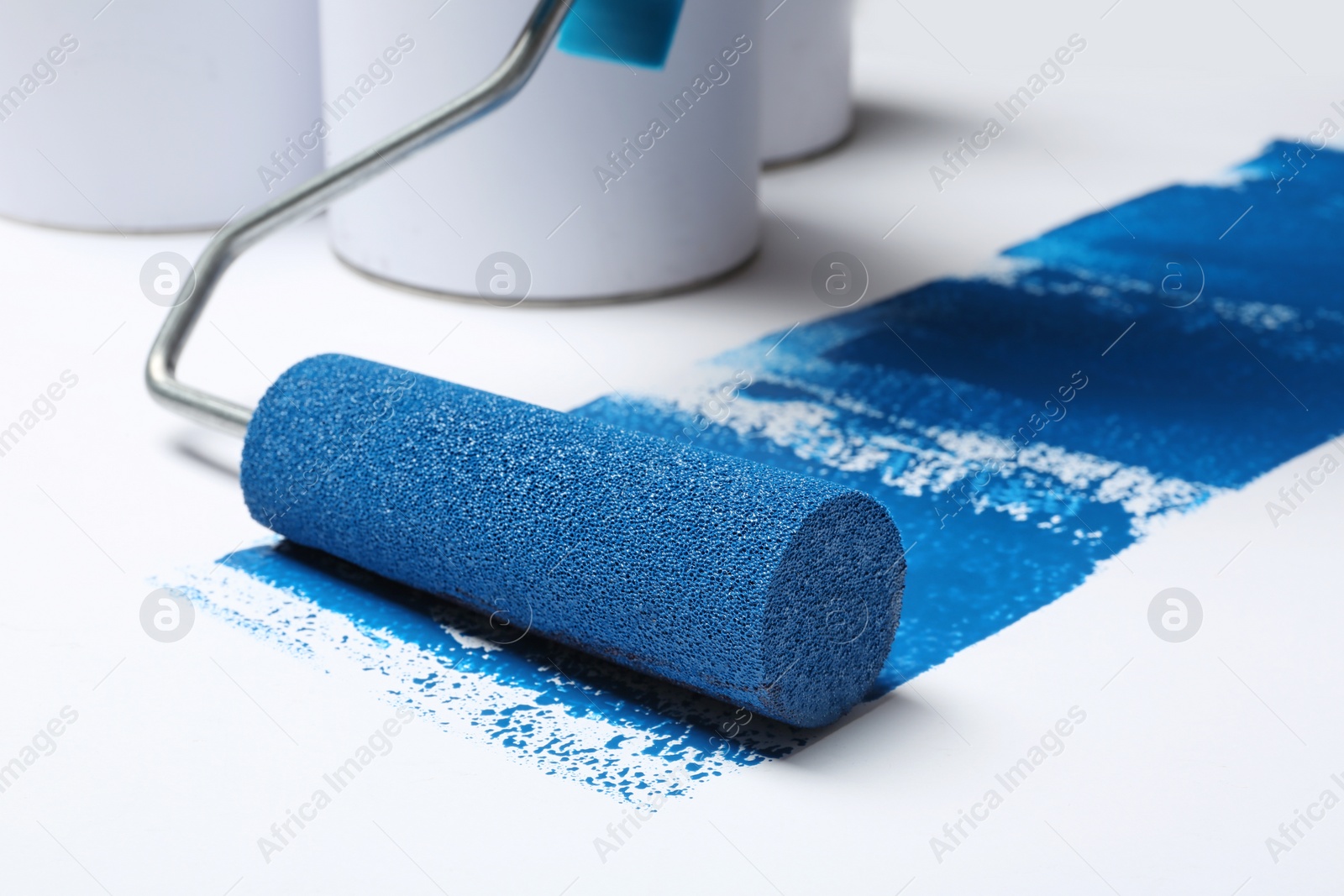 Photo of Roller brush with blue paint near cans on white background