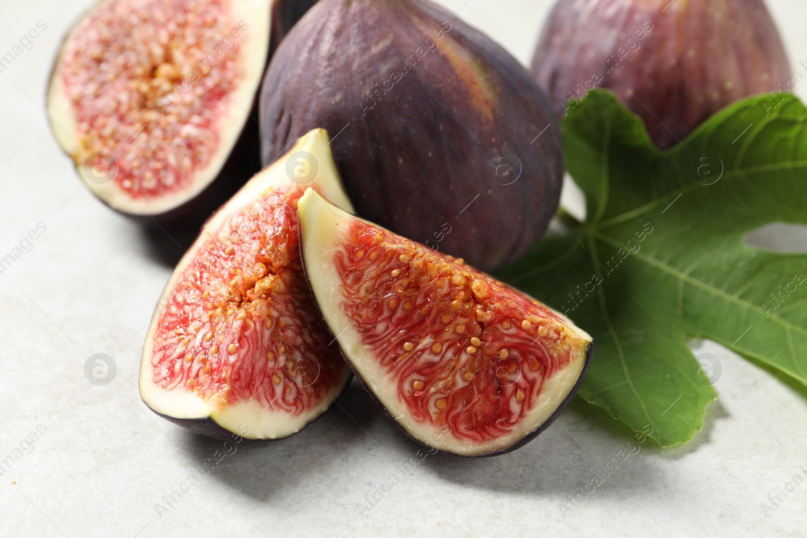 Photo of Fresh ripe figs and green leaf on light table, closeup