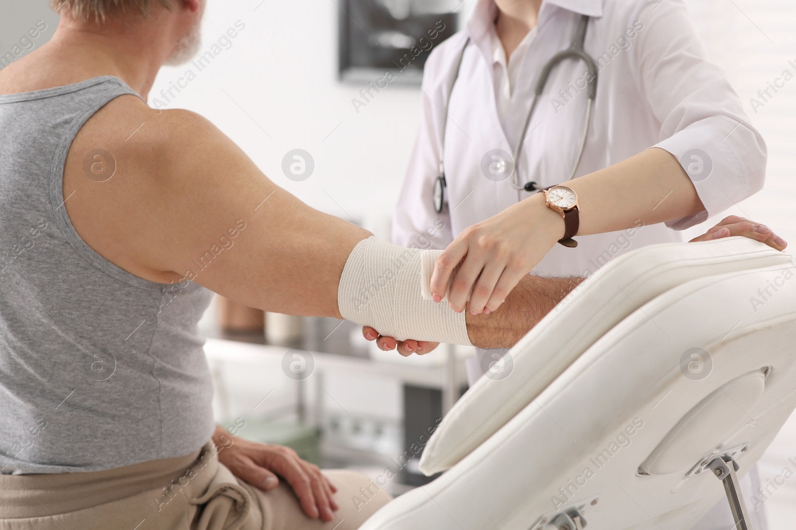 Photo of Orthopedist applying bandage onto patient's elbow in clinic, closeup