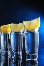 Photo of Shot glasses of vodka with lemon slices on dark blue background