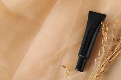 Tube of skin foundation and decorative plants on beige tulle fabric, flat lay with space for text. Makeup product