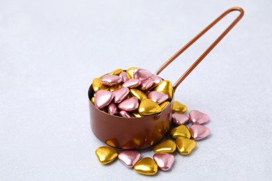 Metal scoop and delicious heart shaped candies on white table