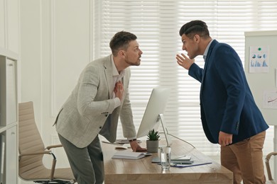 Photo of Colleagues fighting at table in office. Workplace conflict