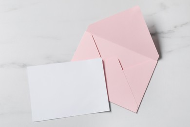 Photo of Blank sheet of paper and letter envelope on white marble table, top view