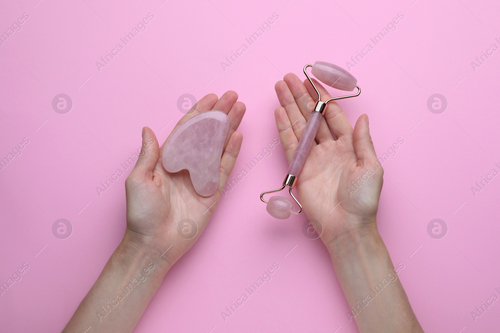 Photo of Woman holding gua sha tool and face roller on pink background, top view