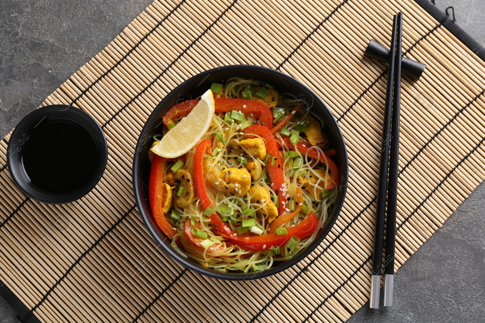 Photo of Stir-fry. Delicious cooked noodles with chicken and vegetables in bowl served on gray textured table, flat lay