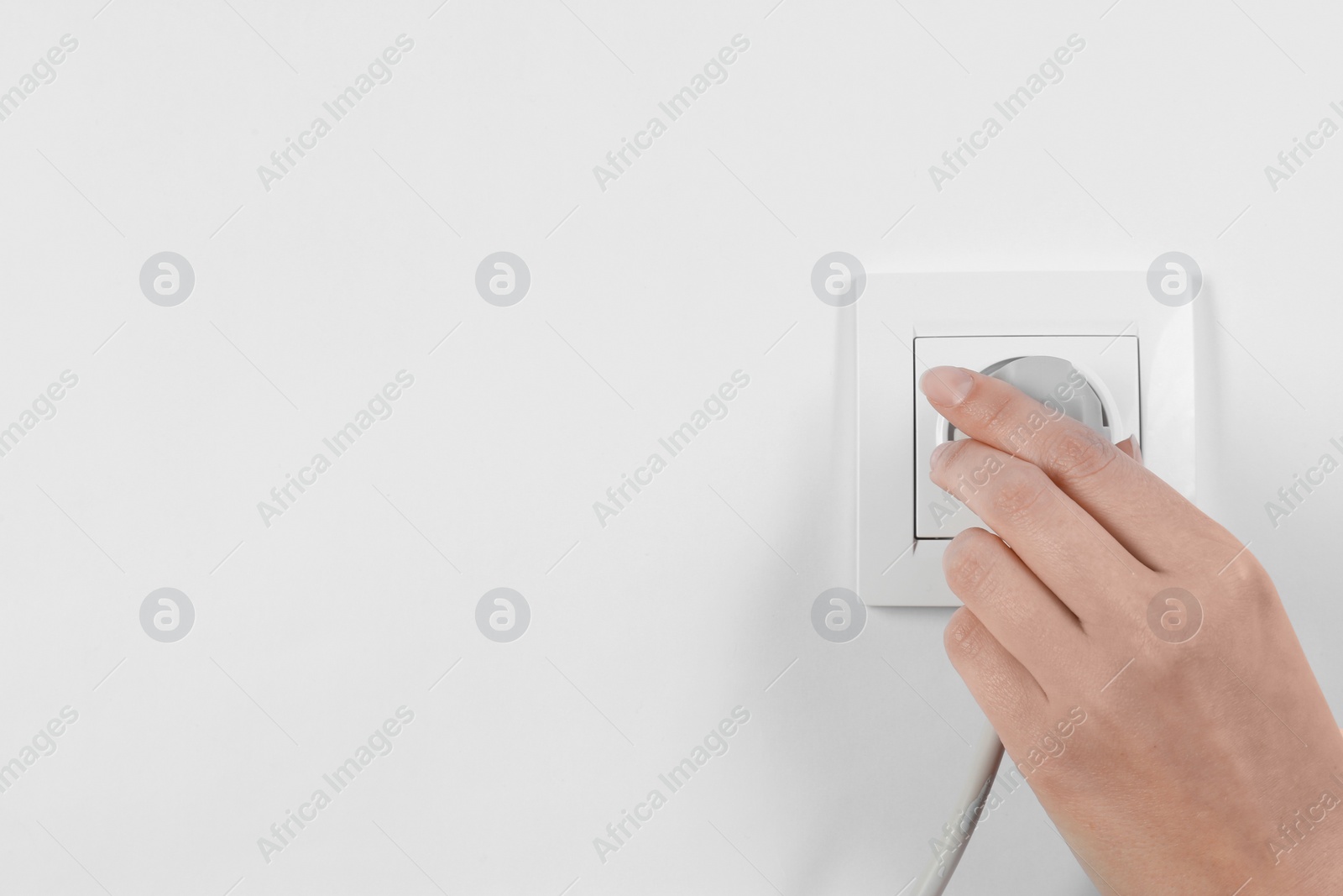 Photo of Woman putting plug into power socket on white background, closeup. Electrician's equipment