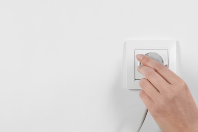 Photo of Woman putting plug into power socket on white background, closeup. Electrician's equipment