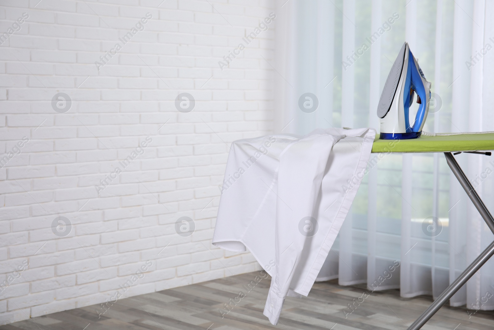 Photo of Modern iron and clean shirt on board indoors, space for text