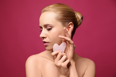 Photo of Beautiful young woman doing facial massage with gua sha tool on pink background