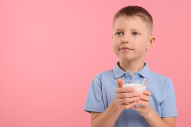 Photo of Cute boy with glass of fresh milk on pink background, space for text