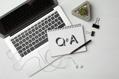 Photo of Notebook with text Q&A and laptop on white wooden table, flat lay