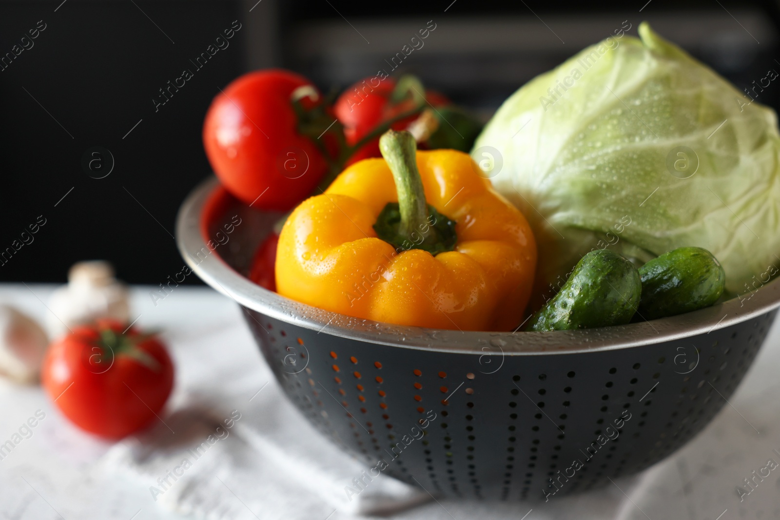 Photo of Metal colander with different wet vegetables on white textured table, closeup