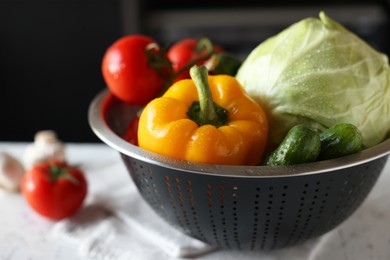Photo of Metal colander with different wet vegetables on white textured table, closeup