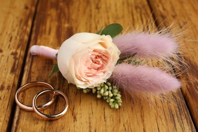 Photo of Small stylish boutonniere and rings on wooden table, closeup
