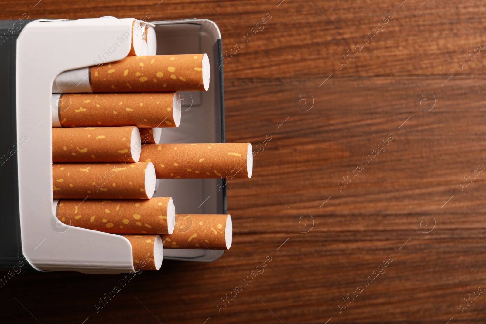 Photo of Pack of cigarettes on wooden table, above view. Space for text