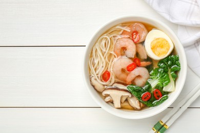 Photo of Tasty ramen with shrimps in bowl and chopsticks on white wooden table, top view. Space for text