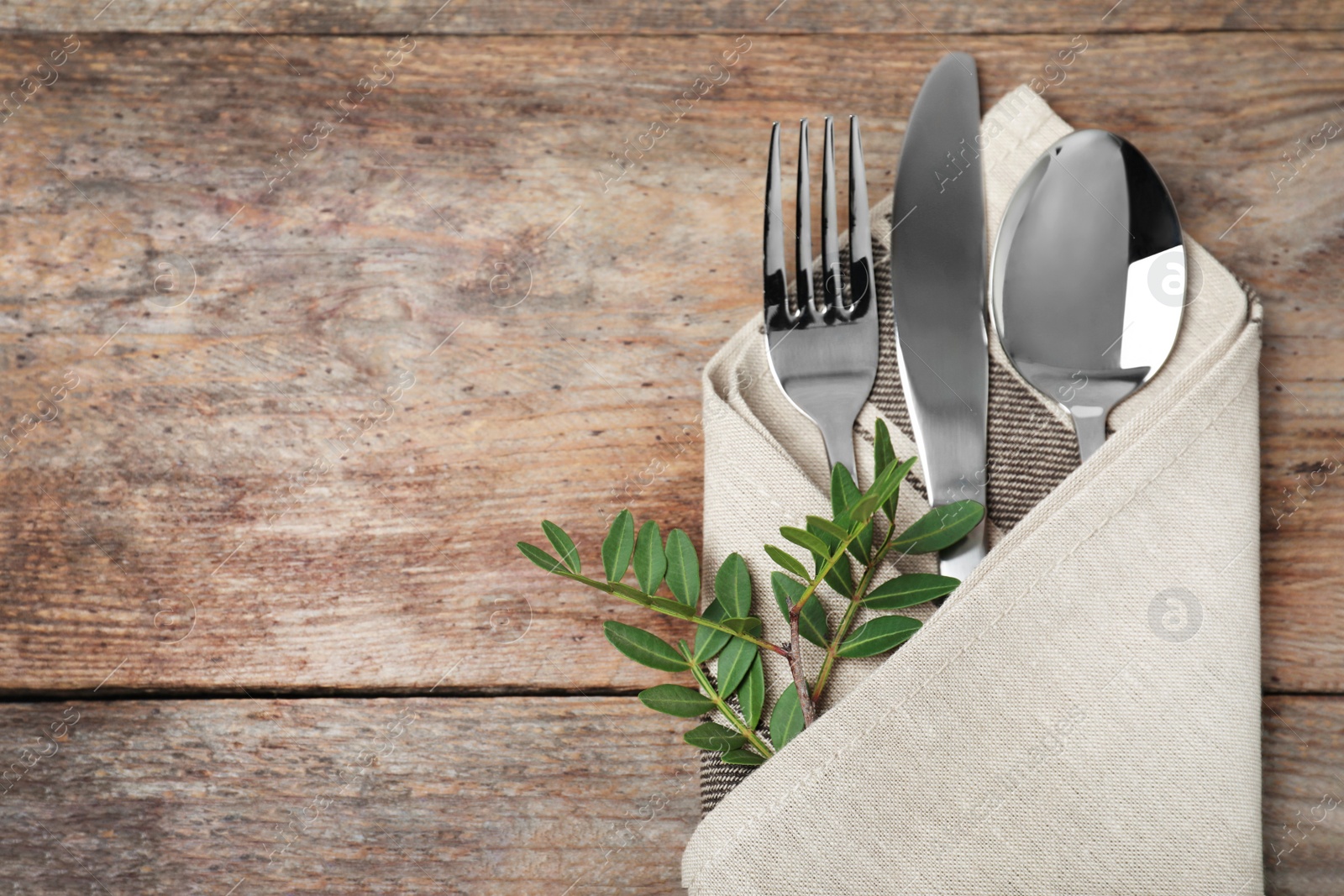 Photo of Folded napkin with fork, spoon and knife on wooden background, top view. Space for text