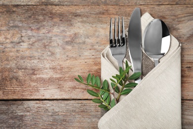 Folded napkin with fork, spoon and knife on wooden background, top view. Space for text