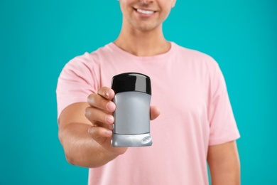 Photo of Young man holding deodorant on blue background, closeup. Mockup for design