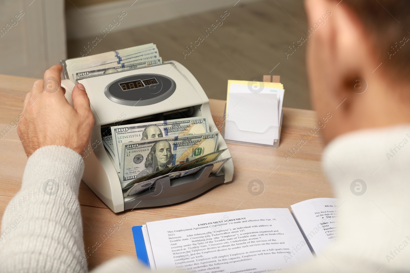 Photo of Man using banknote counter at wooden table indoors, closeup