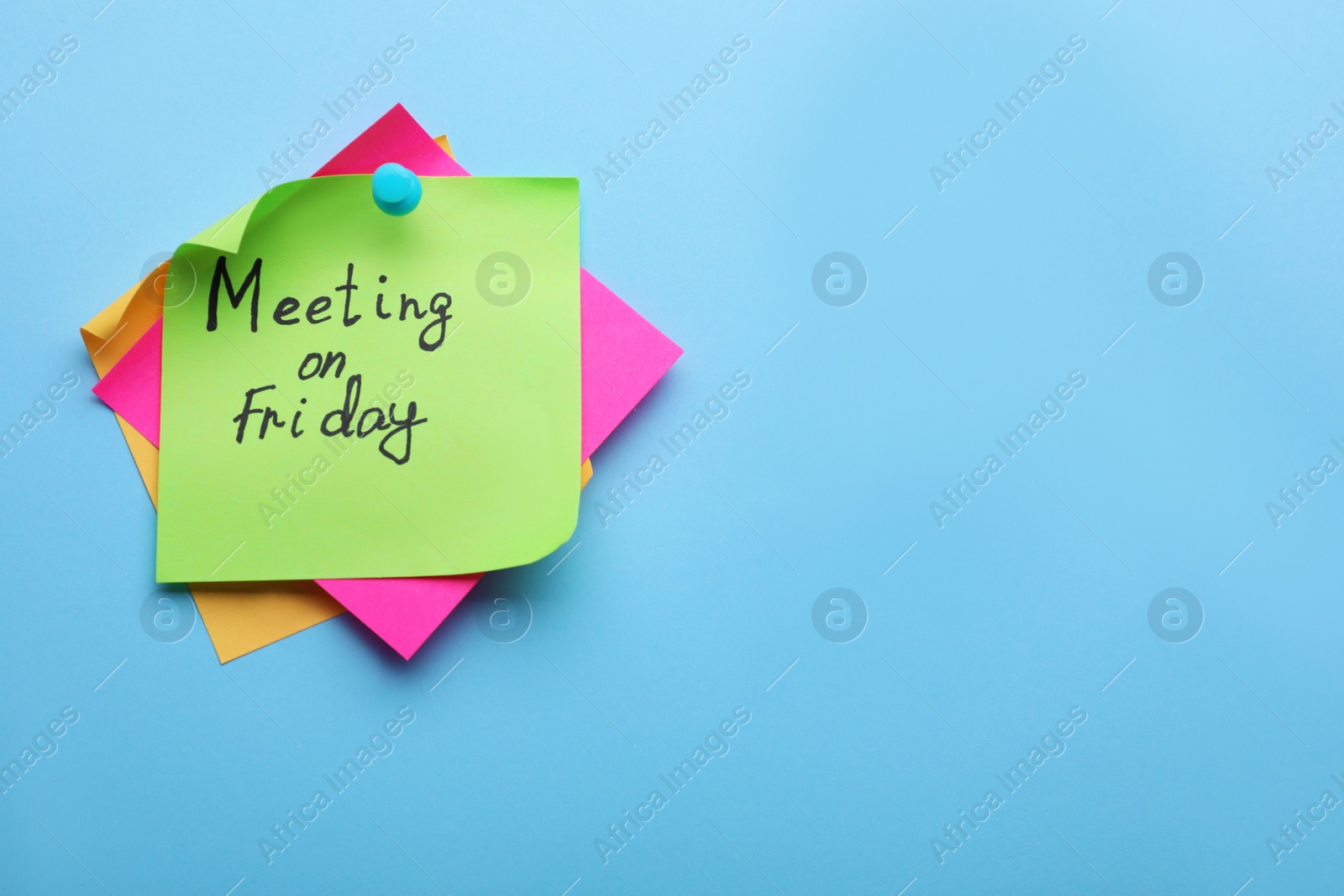 Photo of Paper note with words Meeting on Friday pinned against light blue background, space for text