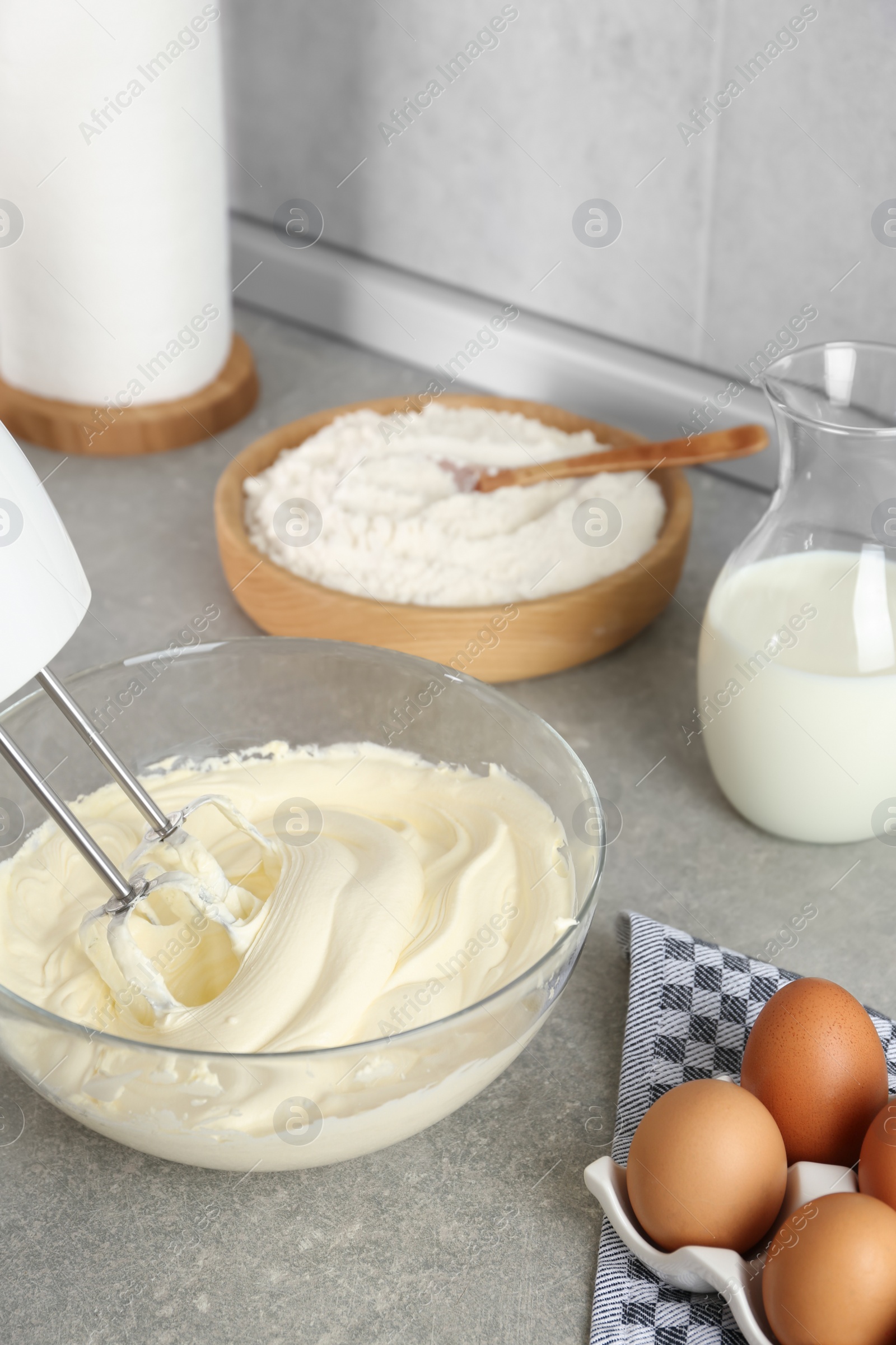 Photo of Whipping white cream in glass bowl with mixer on light grey table