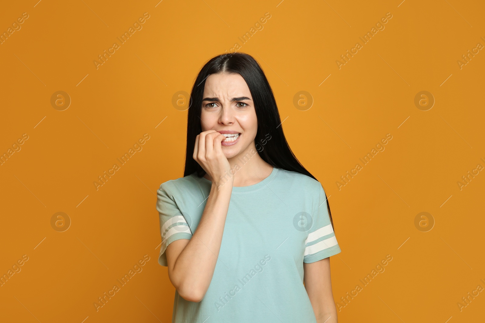 Photo of Young woman biting her nails on yellow background