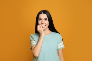 Young woman biting her nails on yellow background