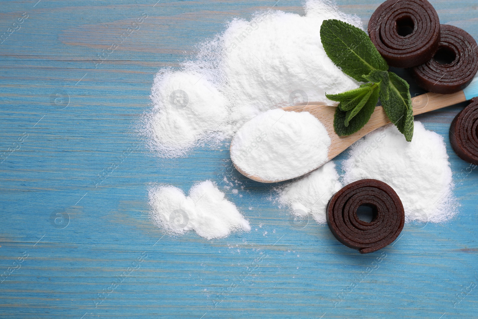 Photo of Sweet fructose powder, mint leaves and fruit leather rolls on light blue wooden table, flat lay. Space for text