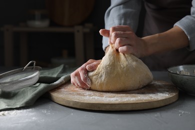 Woman kneading dough at grey table, closeup