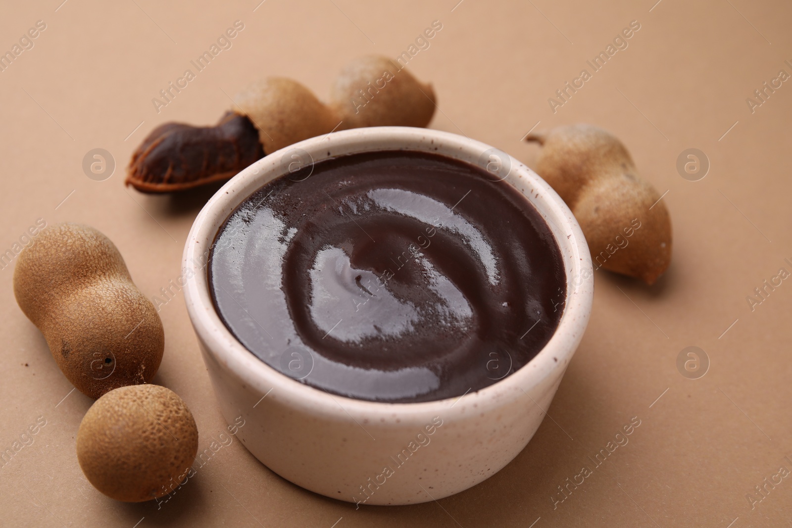 Bowl of tamarind sauce and fresh pods on light brown table, closeup Photo of Bowl of tamarind sauce and fresh pods on light brown table, closeup