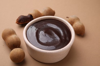 Photo of Bowl of tamarind sauce and fresh pods on light brown table, closeup